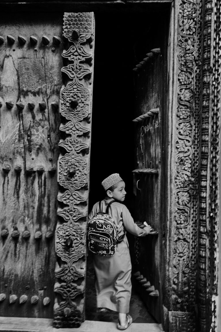 Enfant poussant la porte sculptée d'une maison de Stonetown à Zanzibar