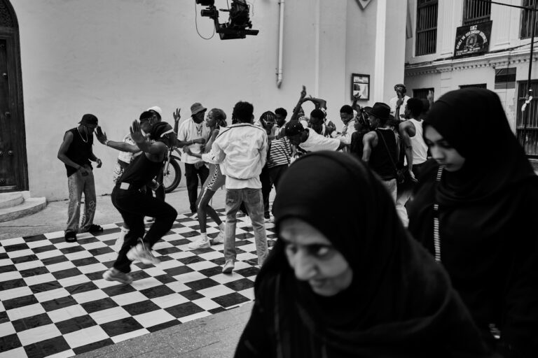 Femme voilée passant devant un groupe de jeunes dansant dans une rue de Stonetown à Zanzibar